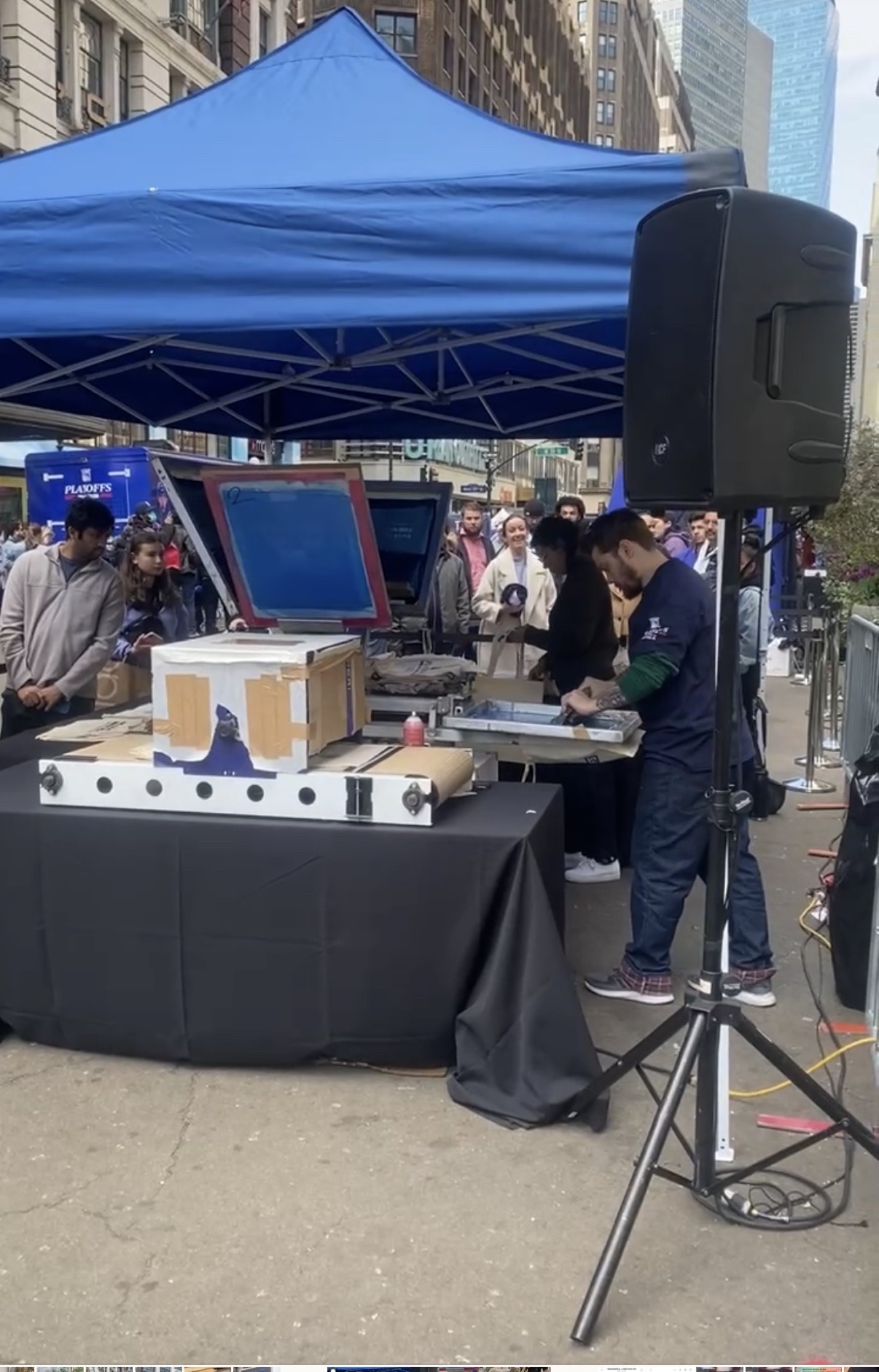 The outdoor tent setup at Herald Square for the Knicks playoffs — press and dryer on the table, crowd watching