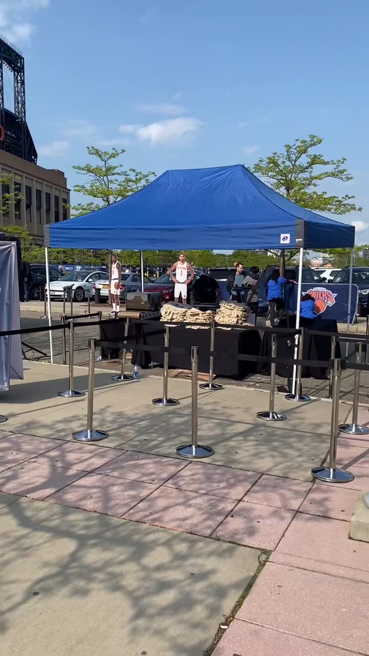 The Knicks Tote Bag Press setup outside Citi Field — blue tent, stanchion queue lanes and the Knicks banner