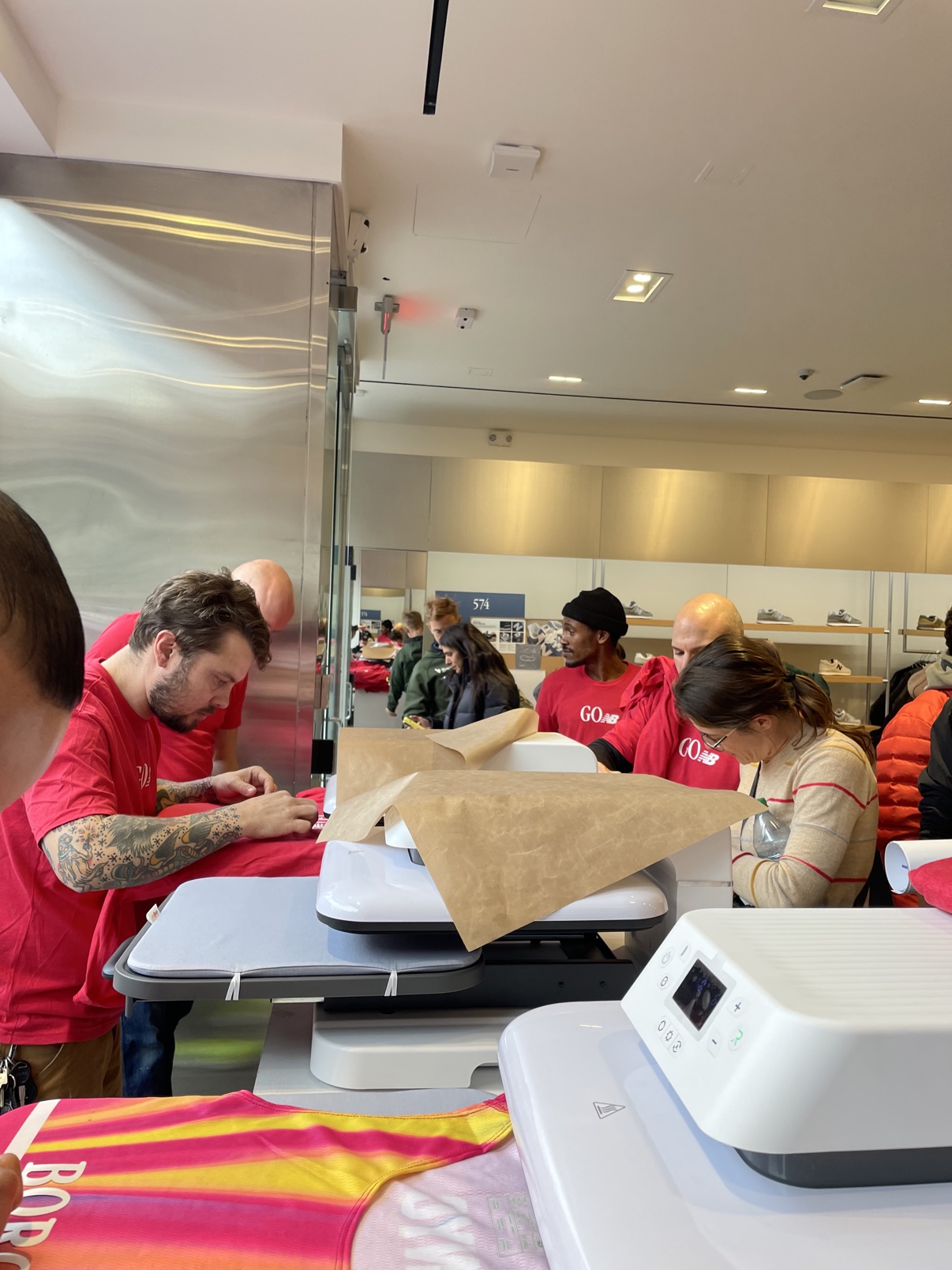 The heat press line inside the New Balance store — crew in red event shirts pressing while customers wait