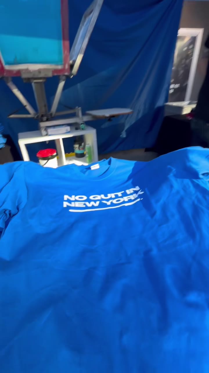 A finished blue Rangers tee reading NO QUIT IN NEW YORK laid out on the table under the press
