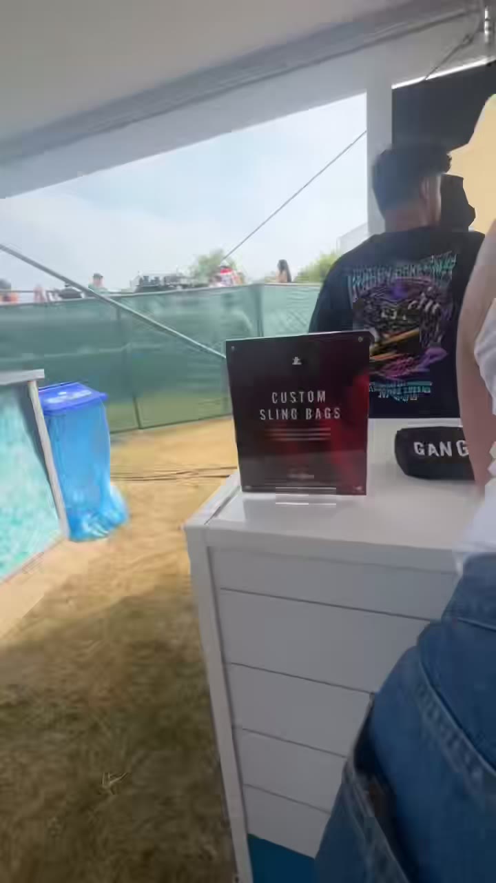 The custom sling bags station at an outdoor summer event — the sign on the counter, guests lining up