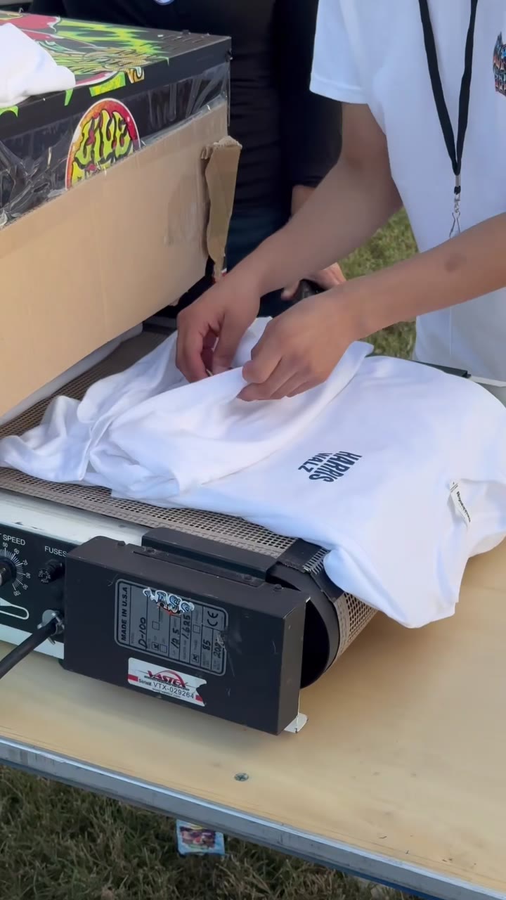 A fresh white Harris/Walz tee coming off the compact dryer at the outdoor rally station