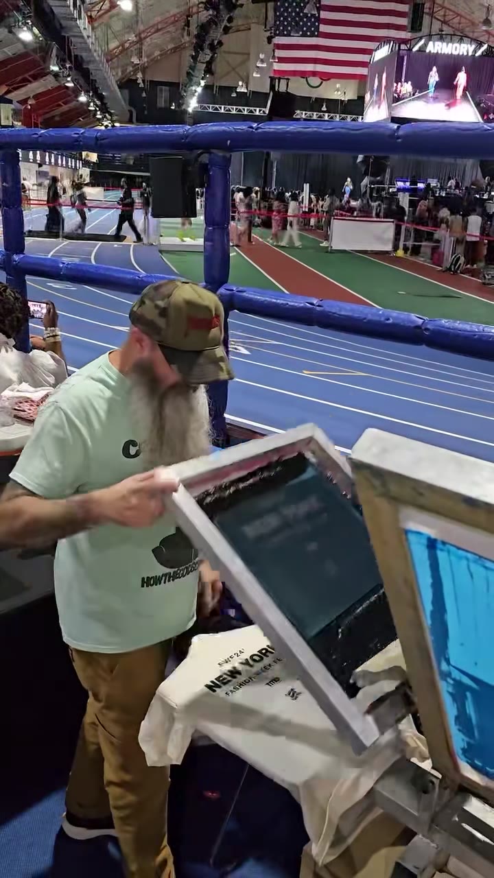 Matt printing totes inside the Armory track venue during Fashion Week Fest, the track and runway behind the press