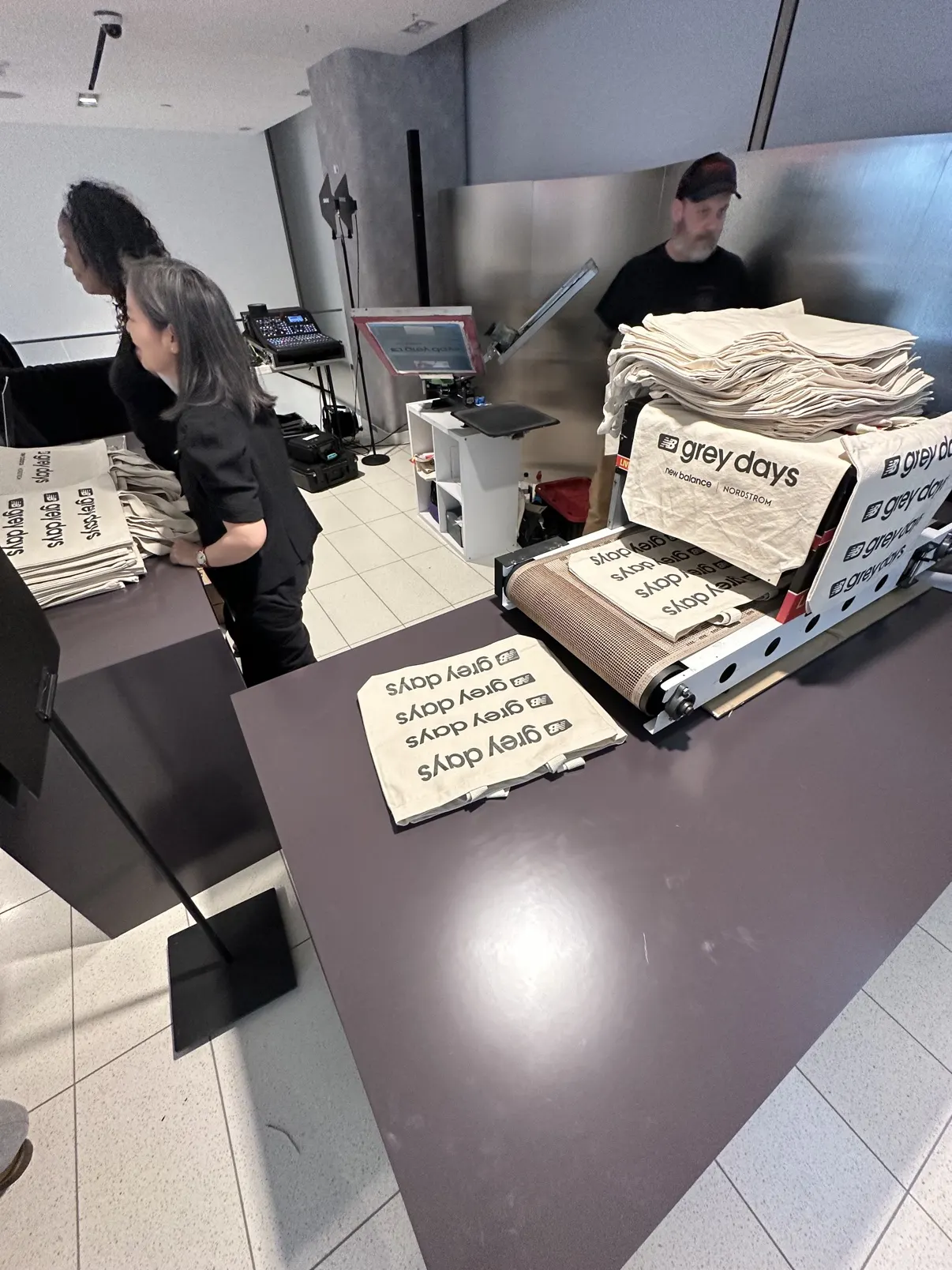 Closer angle of the Grey Days station — totes coming off the dryer belt and stacked high, a crew member behind the counter