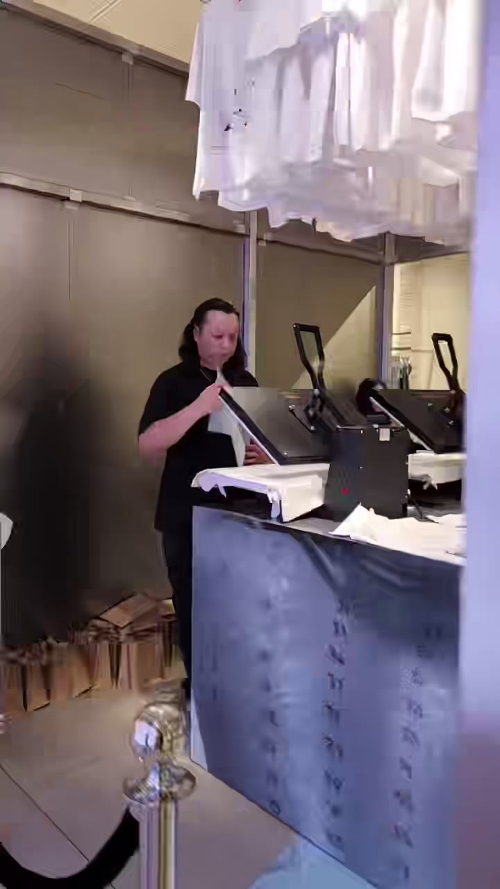 A heat-press station inside a high-end retail space — presses on the counter behind a rope barrier, finished tees hanging above