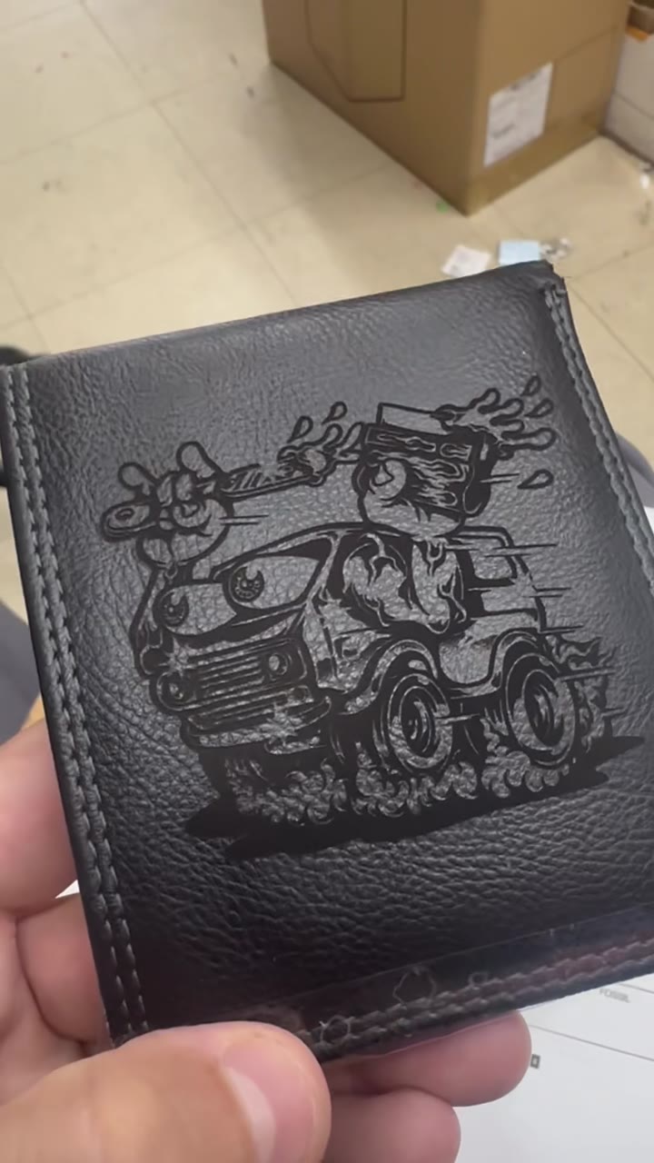 A finished black leather wallet with the hot-rod engraving, held in hand
