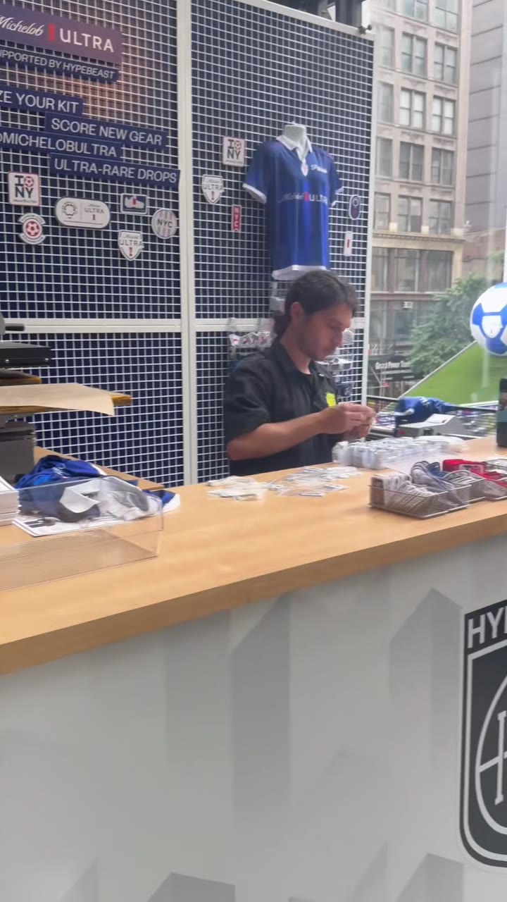 The Hypebeast-supported Michelob Ultra customization booth — grid wall with patches and a jersey, a crew member working the counter at a street-level event